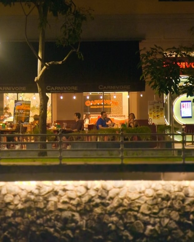 Diners seated under the Carnivore awnings on the riverside walkway at night